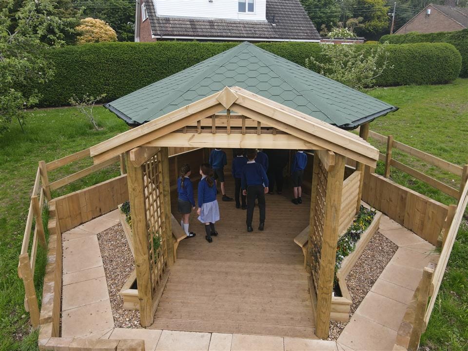 A wooden school gazebo that has been installed with fences around the area, creating a tranquil garden area.