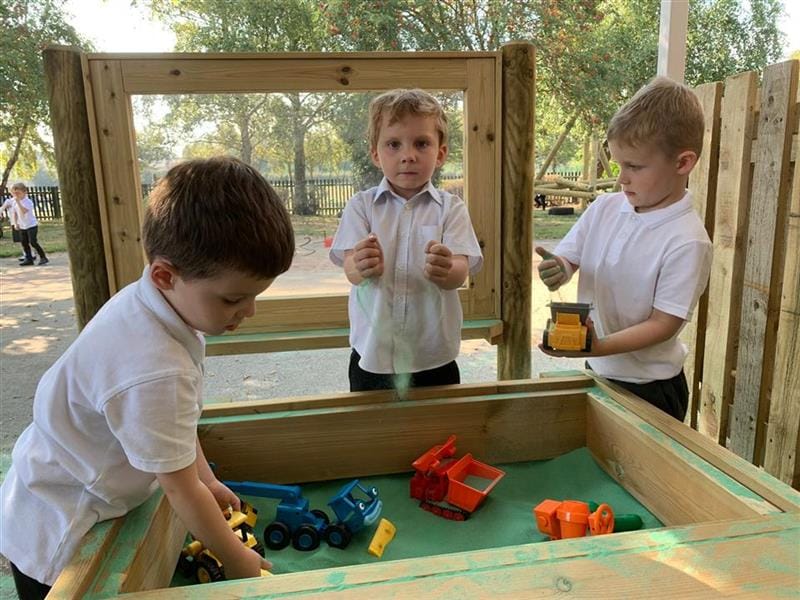 three little boys stand around a construction table and play with blocks and toys in what looks like blue sand