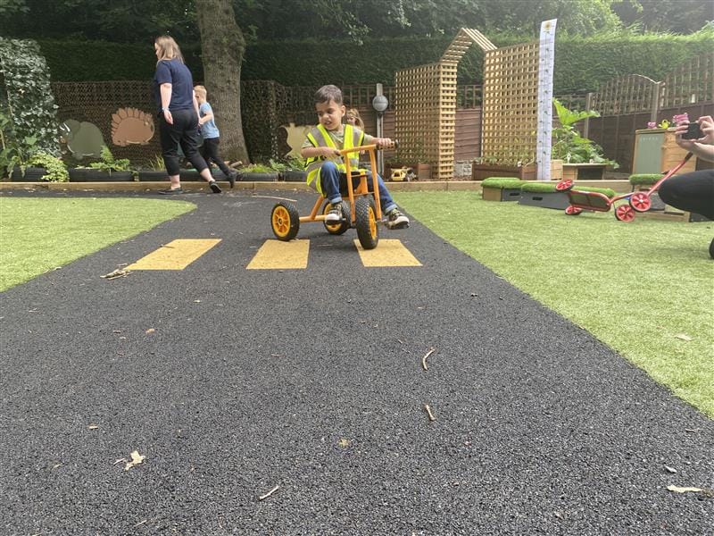 a child scoots along the wetpour roadway on an orange scooter