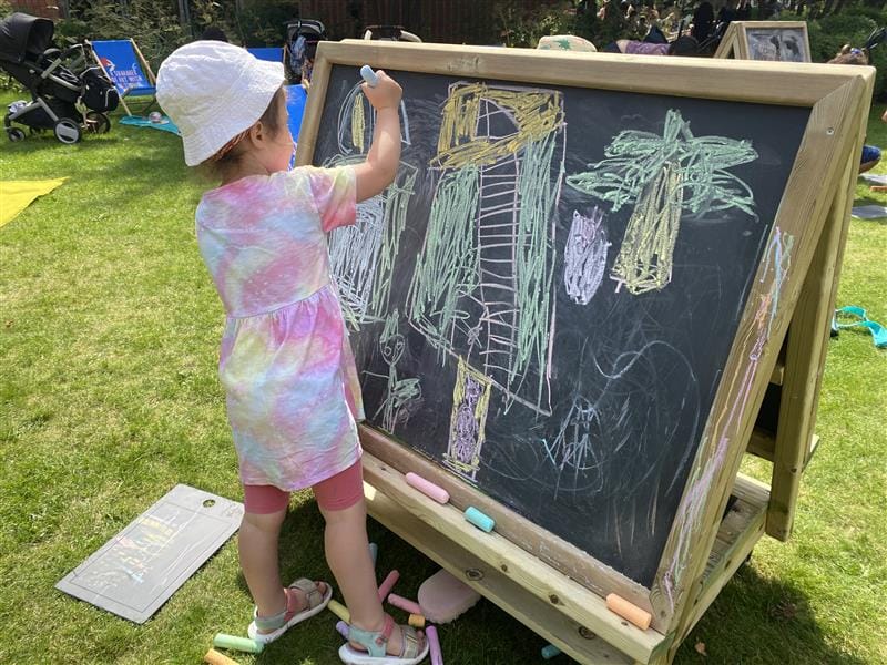 a child stands at the easel and draws on it with coloured chalk