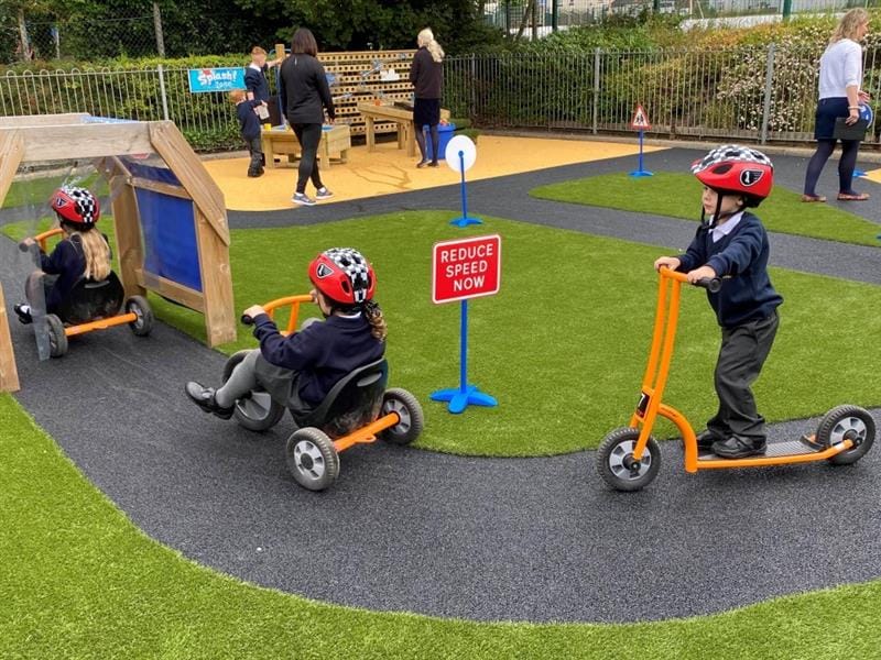 twi children on orange scooters race aroudn the black wetpour roadway