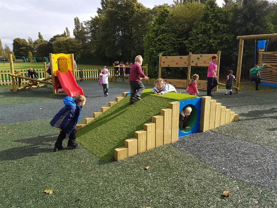 A group of children are playing on a playground with a variety of playground equipment.