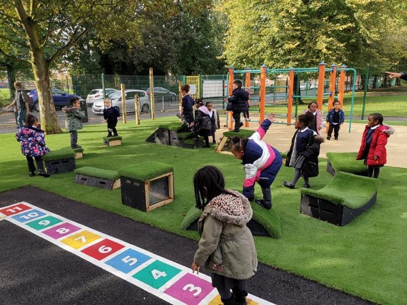 Colourful hopscotch markings that a little girl is jumping along whilst her classmates play in the background