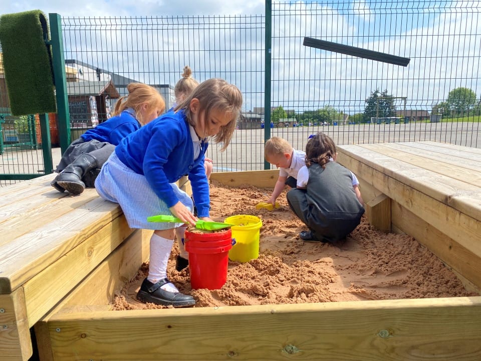 A small group of children are building sand castles in a sandpit whilst it's sunny.
