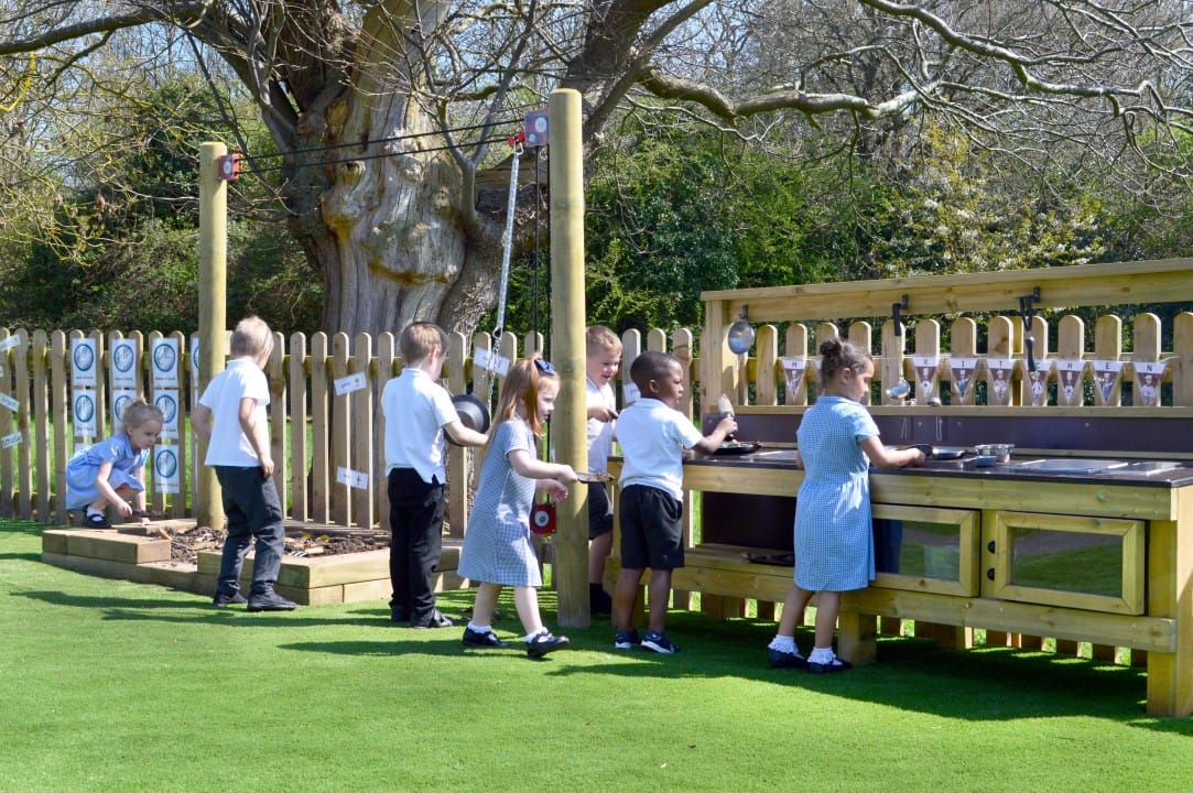 A group of children are playing with different pieces of playground equipment, which revolves around messy play.