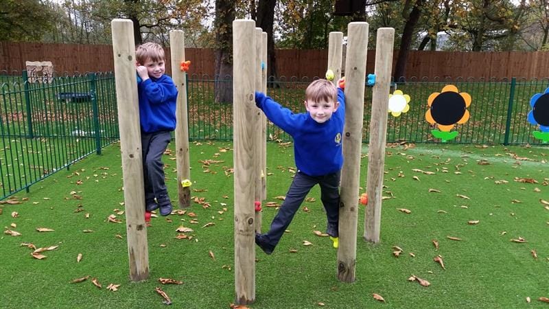 two little boys in blue school uniform develop their arm strength on the wooden timber climbing poles as they hold on and pose for a picture