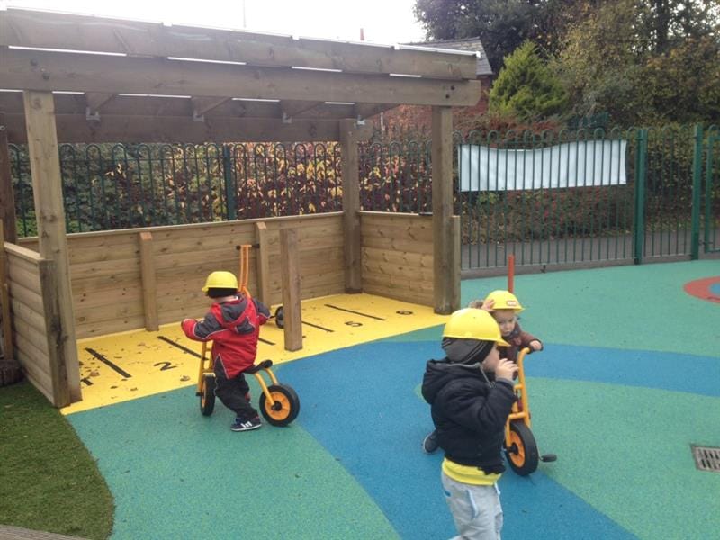 three children playing with the trikes and pushing them into the storage area