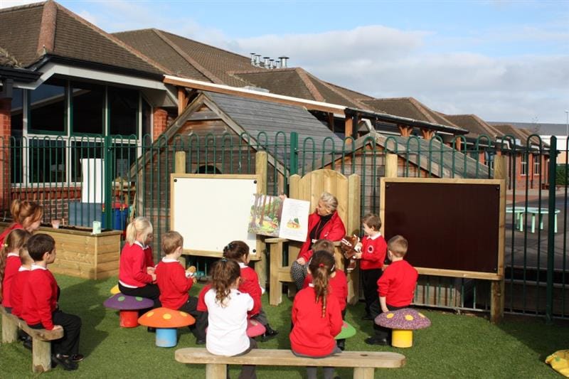 a teacher sits in the storytelling chair and shows a picture book to the pupils sitting on the perch benches 