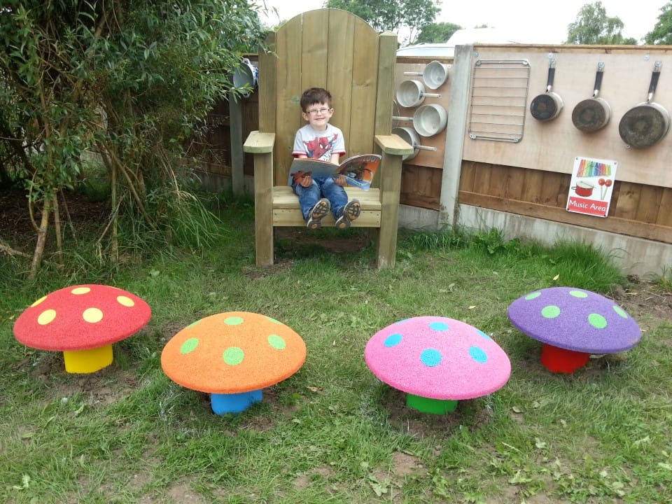 a little boy sits ont he timber storytelling chair reading a book with the mushroom seats in front of him