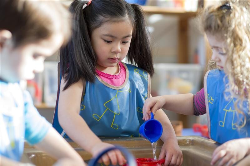 three children play with shapes and water whilst they look into a tub