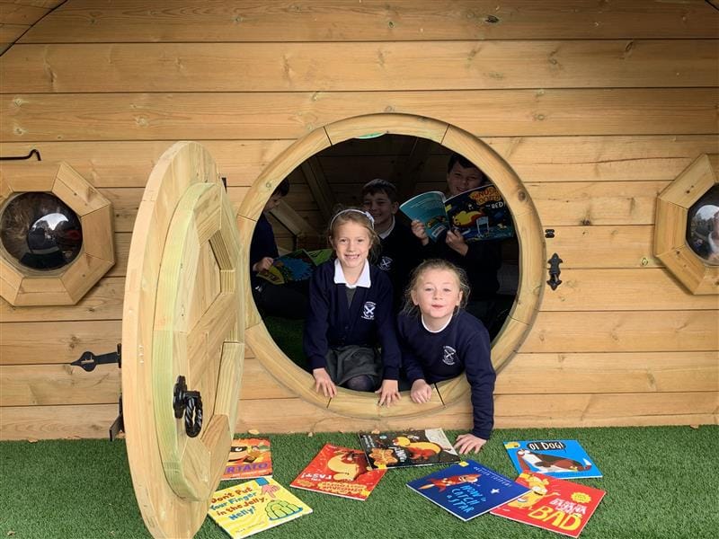 children peek out of the hobbit house and look down at books laid out on the floor in front of them
