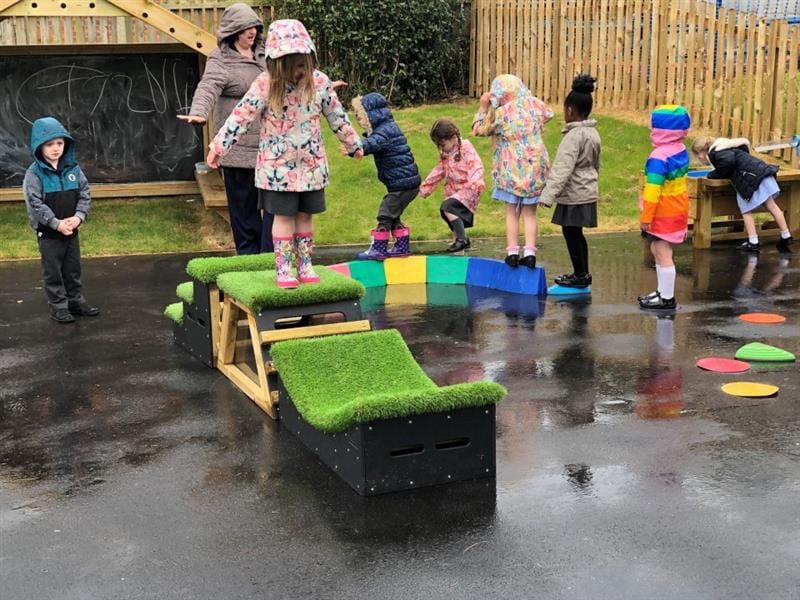 children in raincoats run around on the get set, go blocks with rainy tarmac below