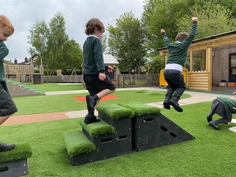 two little boys in green and white and black school uniform run across the grass topped get set go blocks