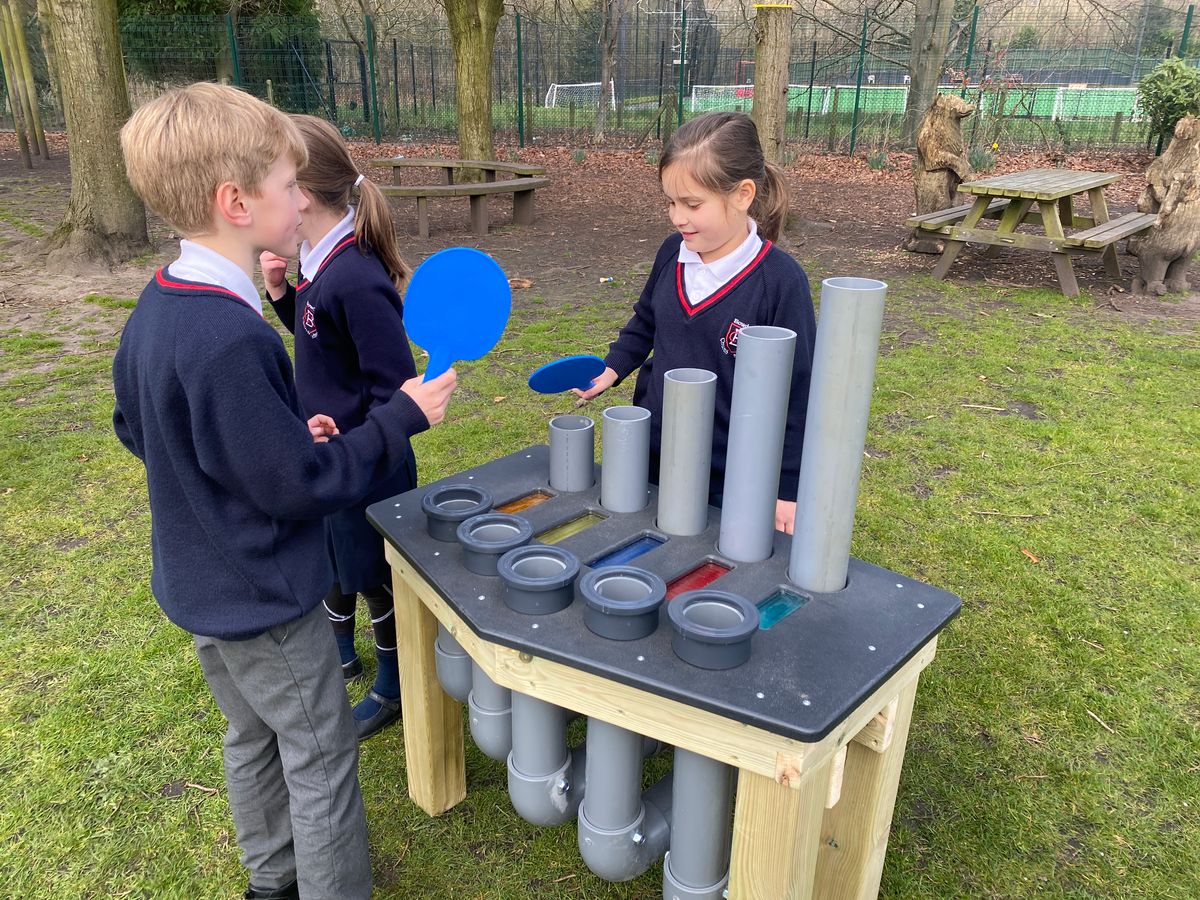 Three children are playing with the freestanding batonka, with two of the children holding plastic paddles.