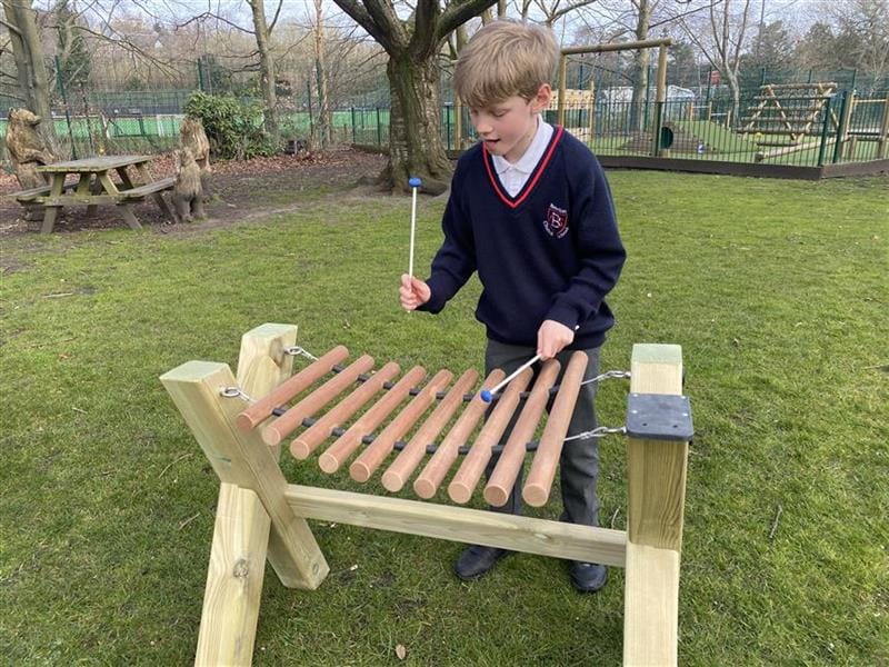 a child stands with two plastic beaters and hit the marimba