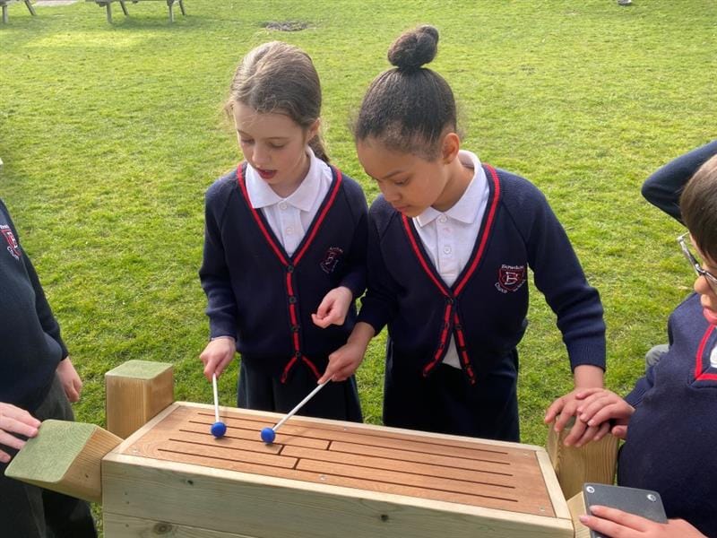 2 children playing tongue drum in their school field