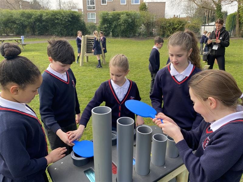 A class of children playing on their group batonka, they are using panels to hit the pipes