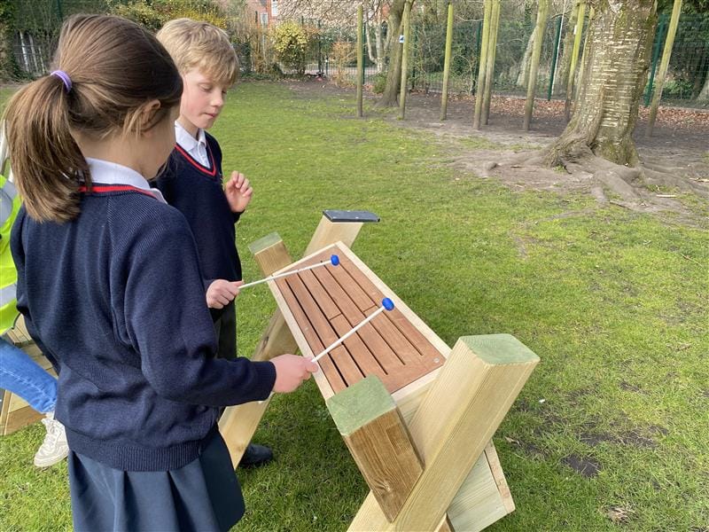 two children stand and beat at the tongue drum