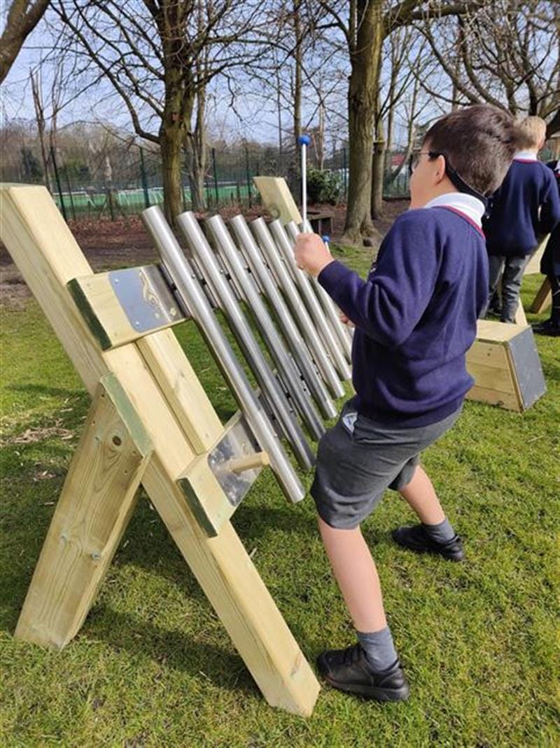 a child stands at the freestanding chimes and plays a tune on the instrument