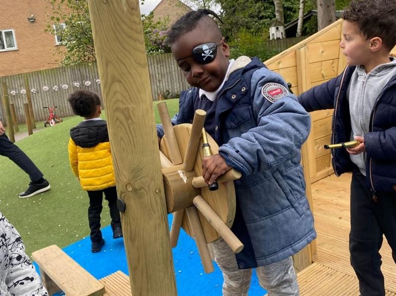 a child stands on the play ship and spins the ship wheel