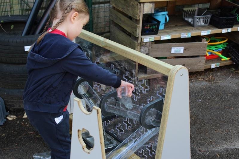 a little girl pours water down the water channels on the early years freestanding water wall