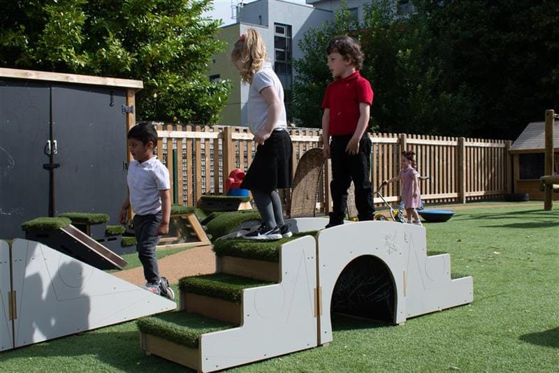 3 children walking over the up and under blocks, one young girl is walking down the stairs