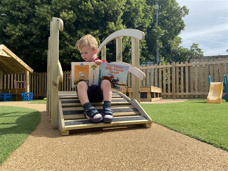 a little boy sits on the end of the bridge and reads a storybook
