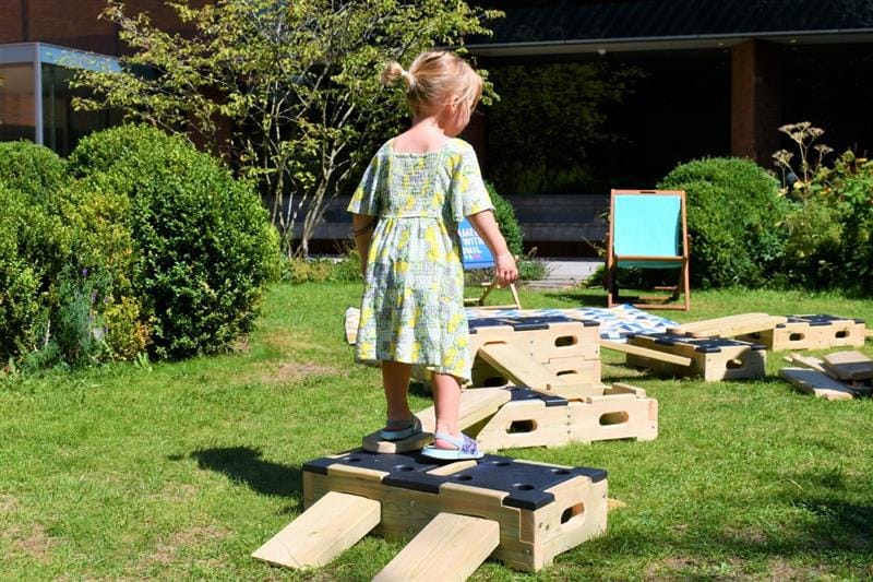 a little girl crosses the play builder trail that is laid out on the grass