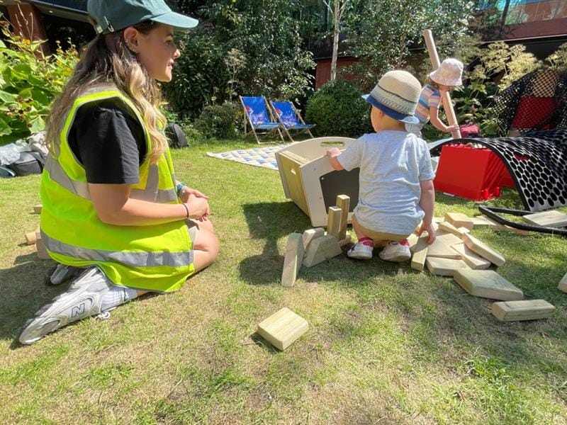 a child sits with a member of pentagon digging in the skip and getting building blocks to build a model