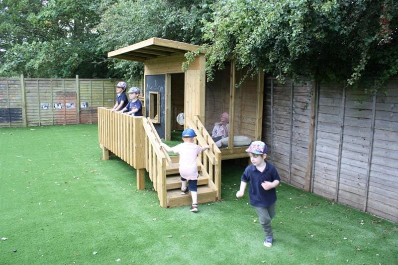 children run around on the artificial grass in front of the lookout den