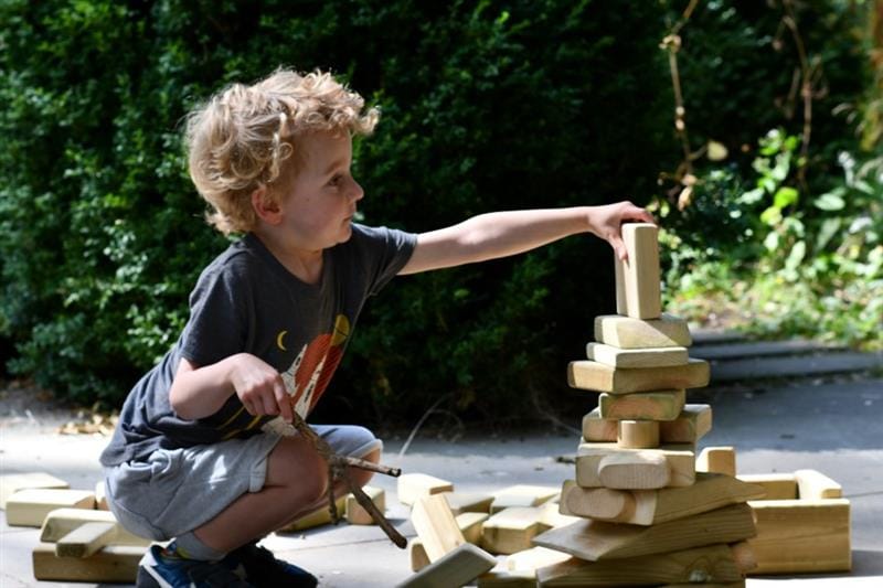 a little boy sits with the wooden blocks from the skip and builds a tower