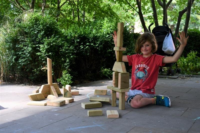 a child shows off a completed tower built with the timber blocks