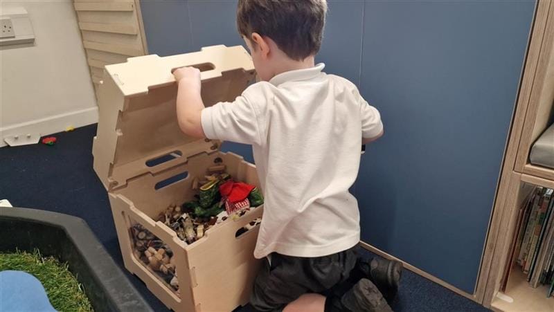 a child sits on the floor and lifts the lid of the stack and sit and reveals storage below