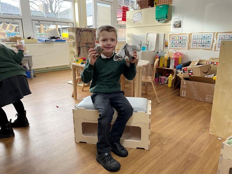 A child sits on the stack and sit and holds onto two toys as he smiles at the camera