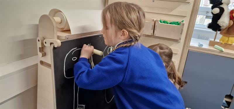 a child kneels in front of the art easel and draws on the board 