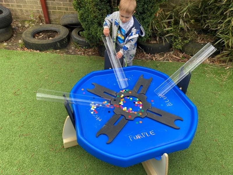 a child stands at the side of the low level tuff spot table and directs counters down the channel