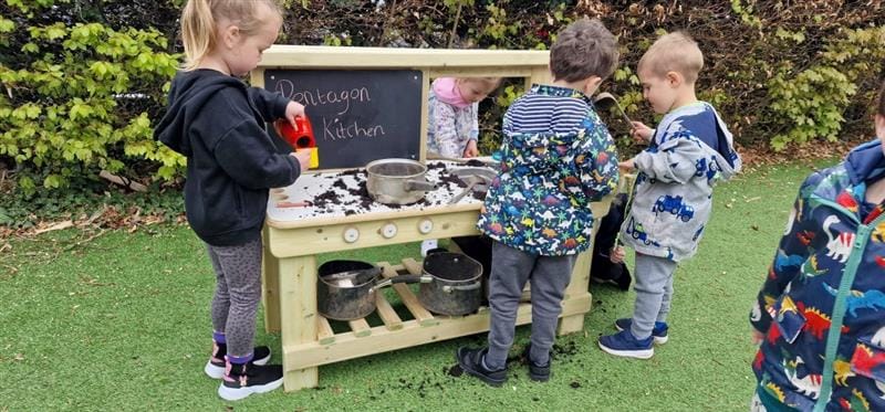 a little girl stands at the mud kitchen and pretends to make a cup of tea