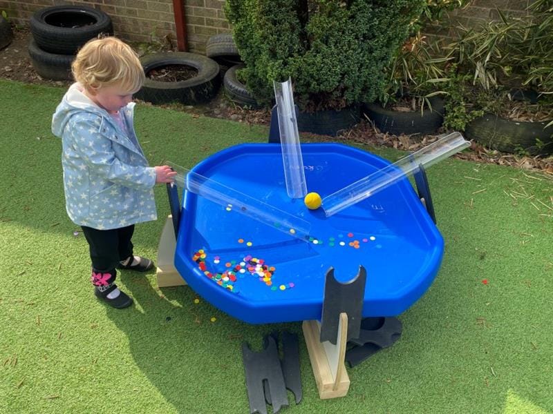 a little girl puts counters down the water channels onto the tuff tray