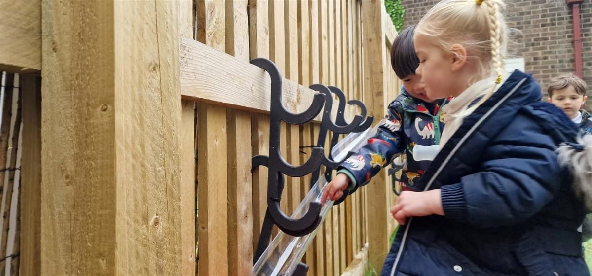 A little girl and boy are pouring water down a plastic tube that is attached to Water Channel Hooks.