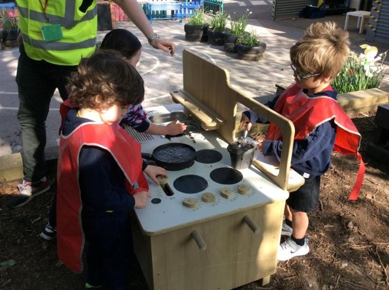 three little children gathered around the mud kitchen