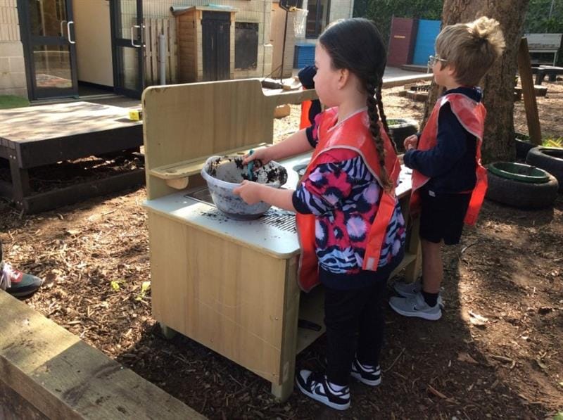 children stand around the mud kitchen and mix mud together