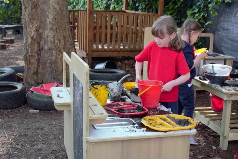 a little girl stands and mixes things together in a bucket 