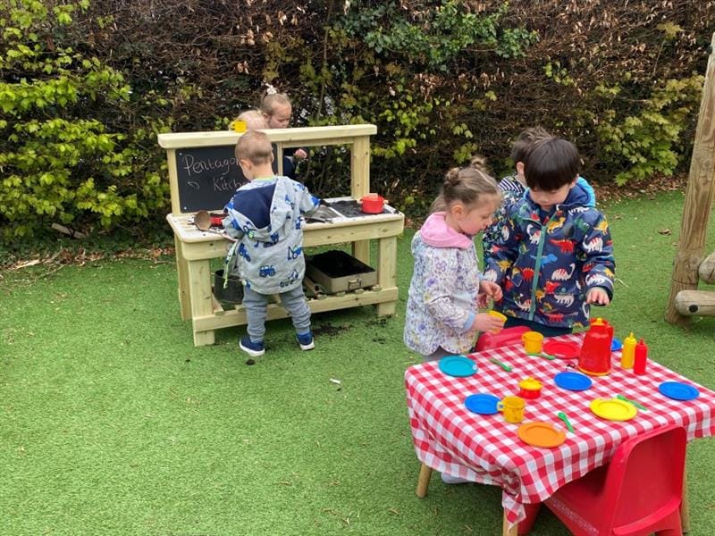 children gather around the mud kitchen and table 
