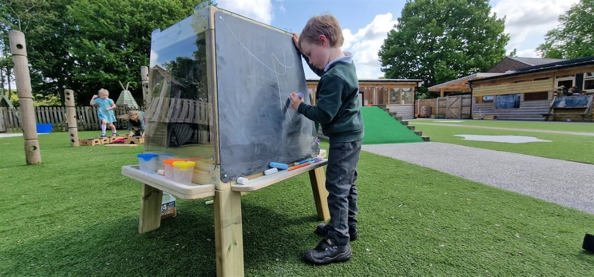 A little boy is drawing on a freestanding chalkboard in the middle of the playground.