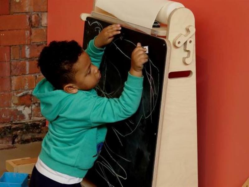 a little boy kneels on the floor and draws on the indoor art easel