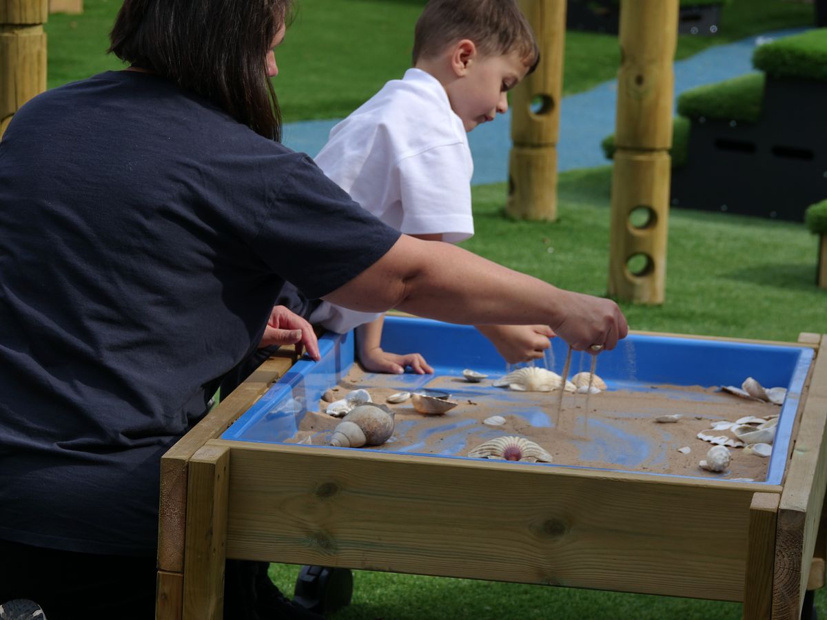 A woman and a boy are grabbing sand and watching it pour into a Sand Table.