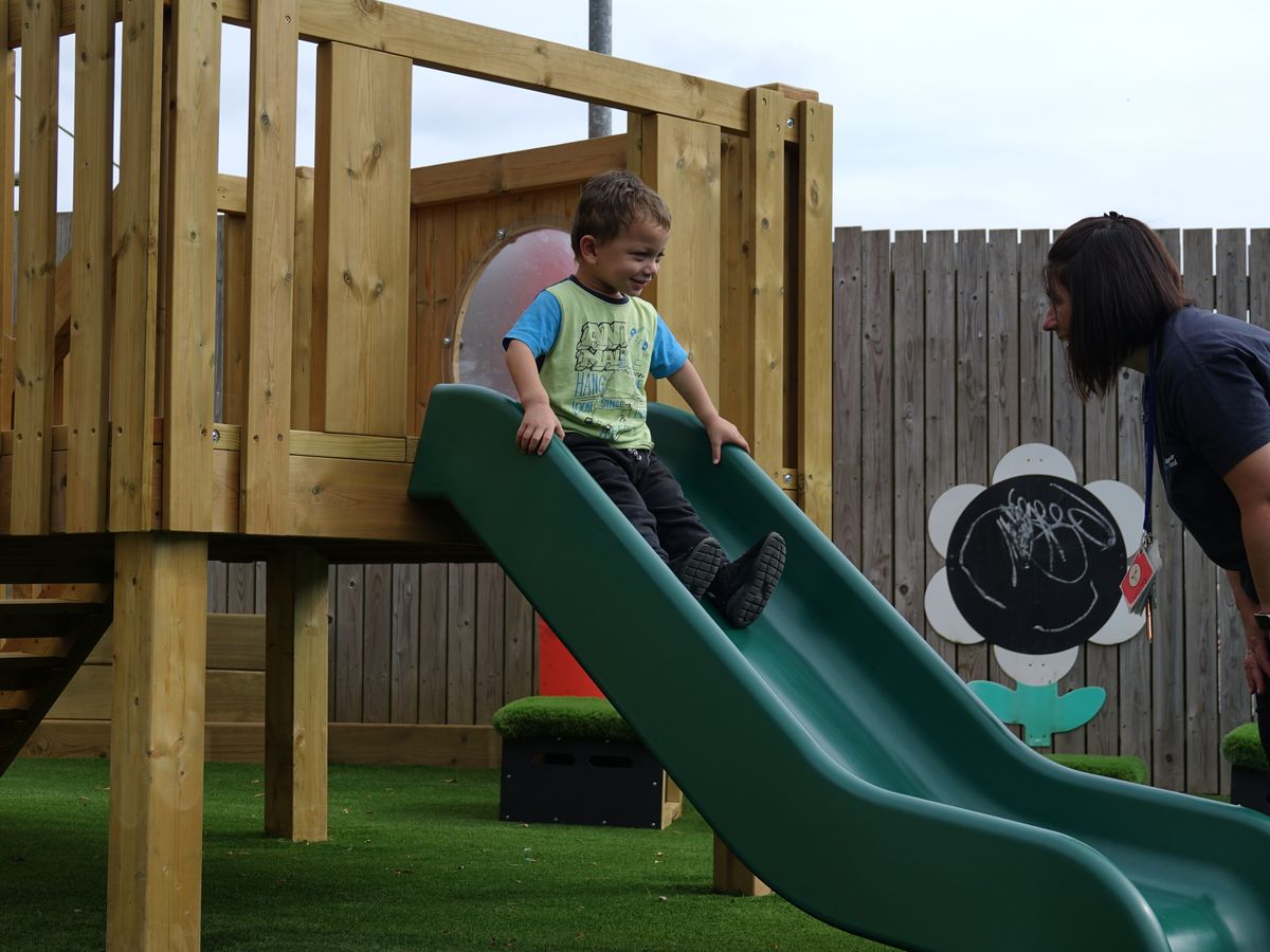 A SEN boy is sliding down a slide towards a SENCO.