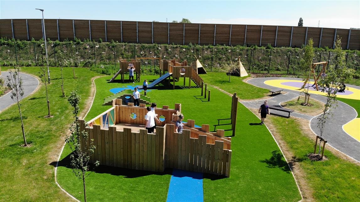 A group of children are stood on top of a play castle, with another play castle facing them.