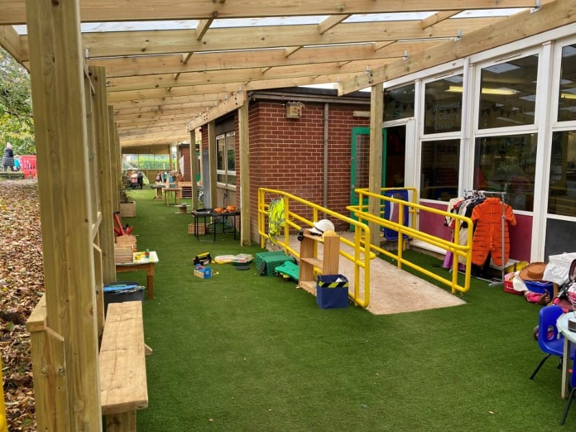 An outdoor canopy that is attached to side of school with a wheelchair ramp that leads to the entrance.