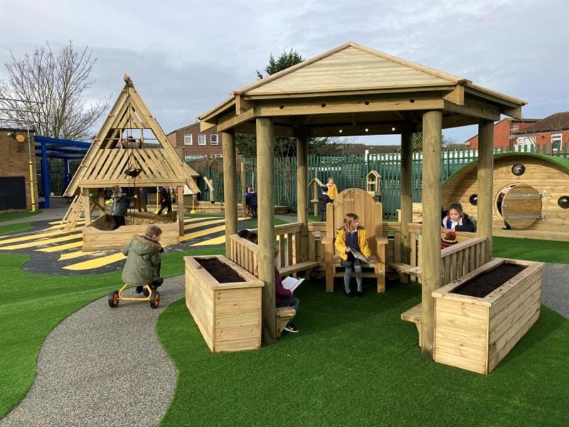 a shot of the gazebo with children sat inside, and a child scoots along the roadway next to the gazebo